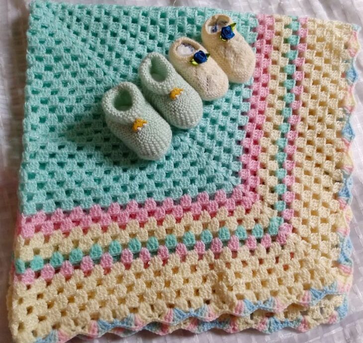 Manta colorida de crochê com sapatinhos de bebê em cima